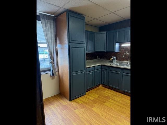 kitchen with sink, light hardwood / wood-style flooring, a paneled ceiling, backsplash, and blue cabinets