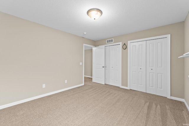 unfurnished bedroom with two closets, a textured ceiling, and carpet