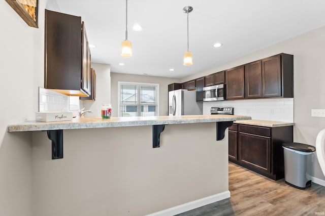 kitchen featuring decorative light fixtures, stainless steel appliances, a breakfast bar, and kitchen peninsula