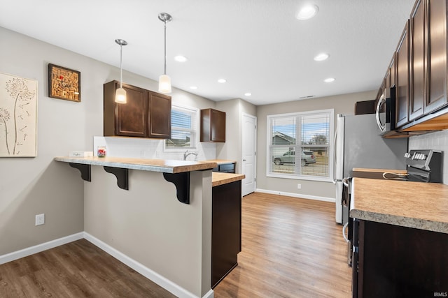 kitchen with a breakfast bar area, backsplash, dark brown cabinetry, decorative light fixtures, and kitchen peninsula