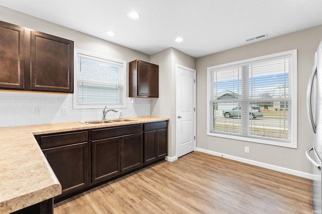 kitchen with dark brown cabinetry, sink, tasteful backsplash, light wood-type flooring, and stainless steel refrigerator