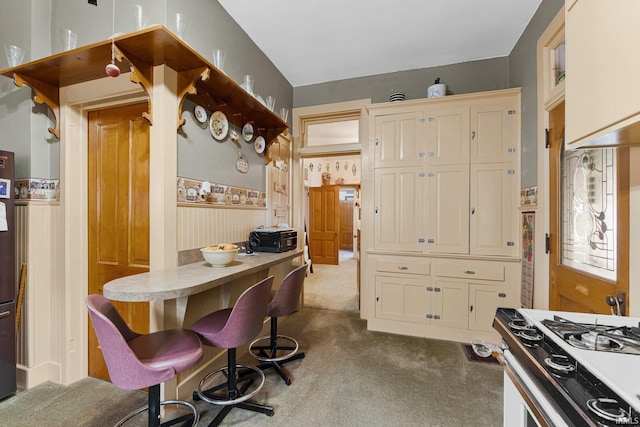 kitchen with cream cabinets, a breakfast bar area, light colored carpet, and gas range gas stove