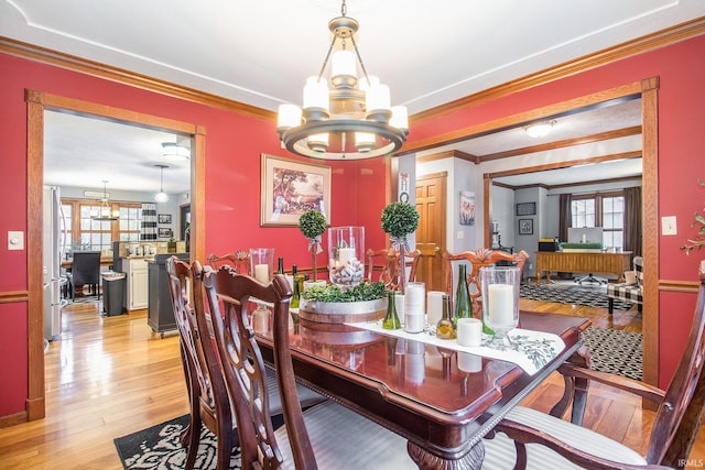 dining room with an inviting chandelier, crown molding, and light wood-type flooring