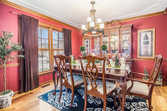 dining area with crown molding, an inviting chandelier, and light wood-type flooring