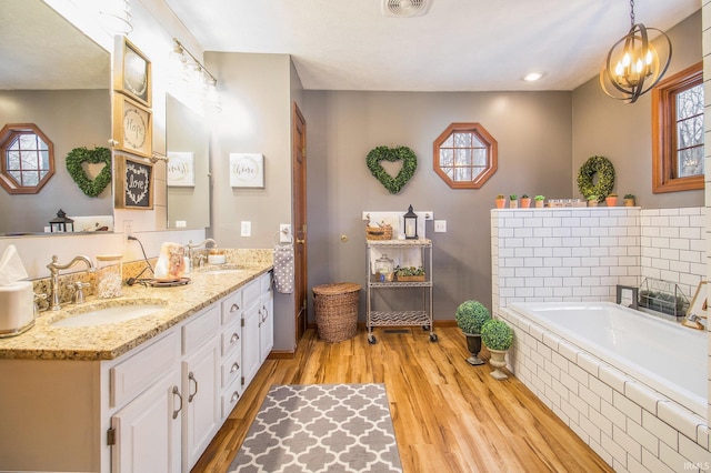 bathroom with tiled tub, wood-type flooring, and vanity