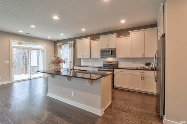 kitchen featuring sink, a breakfast bar area, stainless steel appliances, an island with sink, and white cabinets