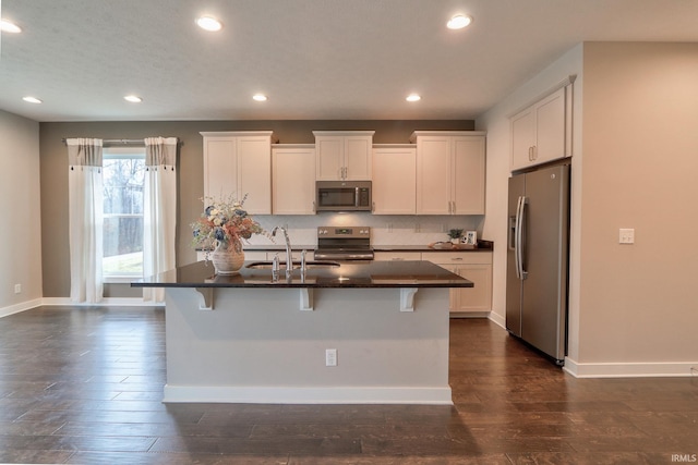 kitchen with a kitchen bar, sink, white cabinetry, appliances with stainless steel finishes, and an island with sink