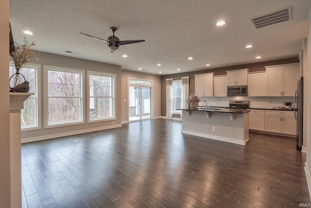 kitchen with an island with sink, appliances with stainless steel finishes, white cabinets, and a kitchen bar