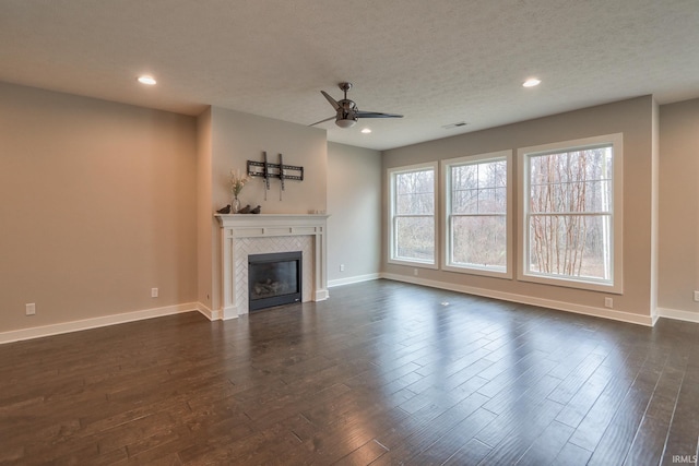 unfurnished living room featuring ceiling fan, a fireplace, dark hardwood / wood-style floors, and a textured ceiling