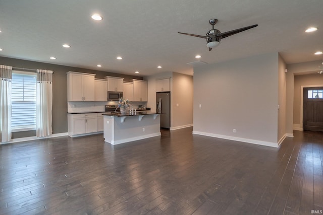 kitchen with a breakfast bar area, white cabinetry, stainless steel appliances, dark hardwood / wood-style floors, and an island with sink