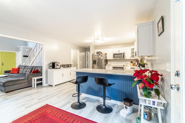 kitchen with a breakfast bar, appliances with stainless steel finishes, light hardwood / wood-style floors, white cabinets, and kitchen peninsula