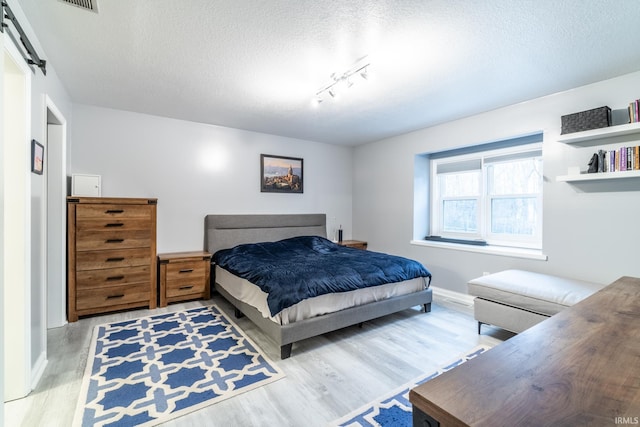 bedroom featuring a barn door, hardwood / wood-style floors, track lighting, and a textured ceiling