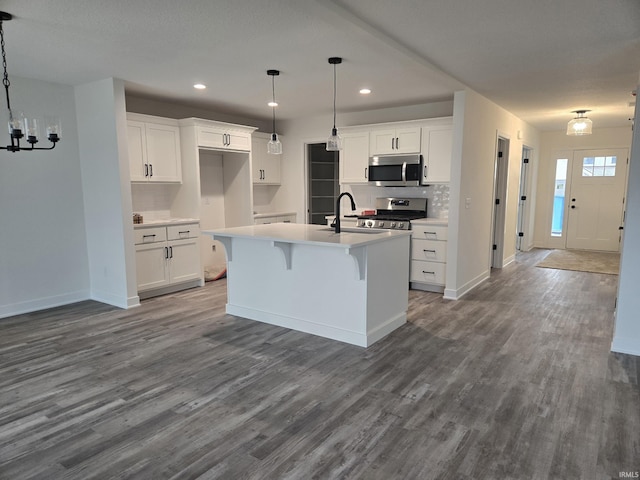 kitchen featuring a center island with sink, hardwood / wood-style flooring, stainless steel appliances, white cabinets, and decorative light fixtures