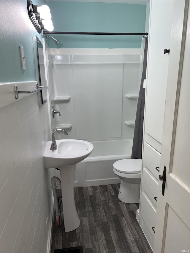 bathroom with wood-type flooring, tile walls, shower / tub combo, and toilet