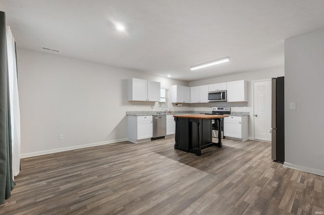 kitchen featuring a breakfast bar, white cabinetry, a center island, appliances with stainless steel finishes, and hardwood / wood-style flooring