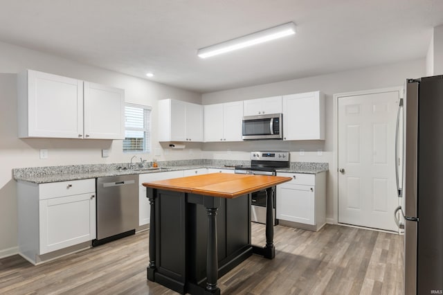 kitchen featuring light wood-type flooring, appliances with stainless steel finishes, a kitchen island, light stone countertops, and white cabinets