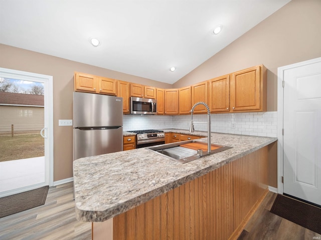 kitchen featuring sink, stainless steel appliances, tasteful backsplash, vaulted ceiling, and kitchen peninsula