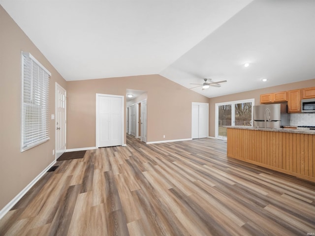 kitchen featuring lofted ceiling, light hardwood / wood-style flooring, stainless steel appliances, decorative backsplash, and light brown cabinets