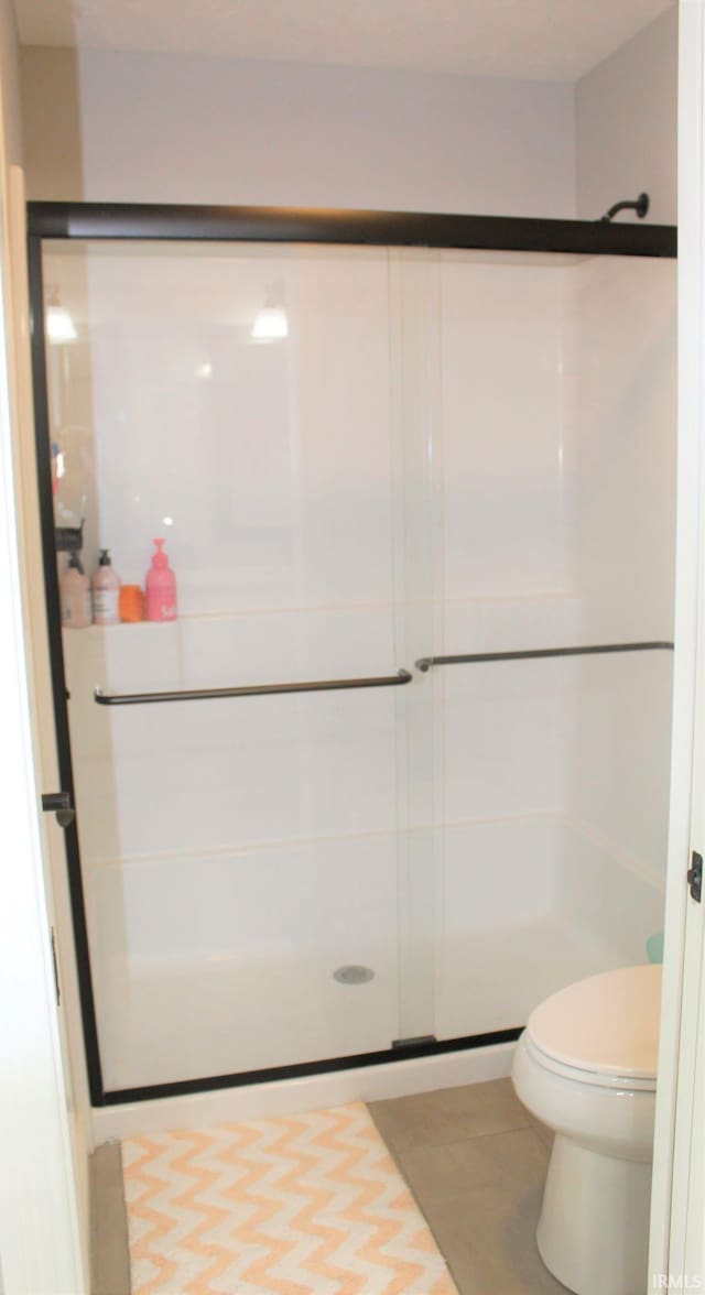 bathroom featuring tile patterned floors, toilet, and an enclosed shower