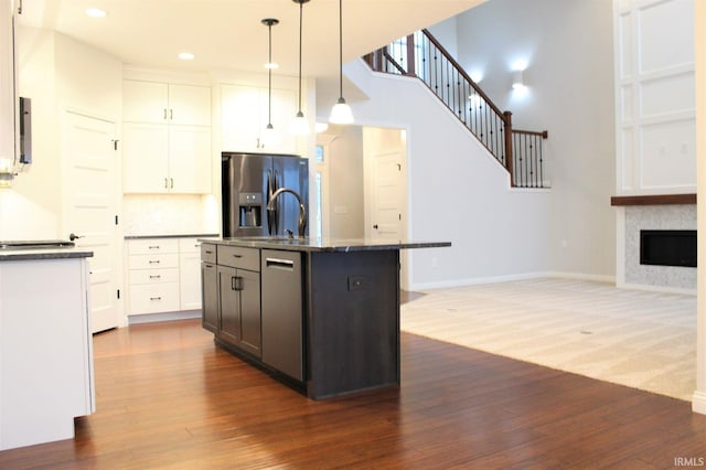 kitchen with dark wood-type flooring, stainless steel fridge with ice dispenser, pendant lighting, a kitchen island with sink, and white cabinets