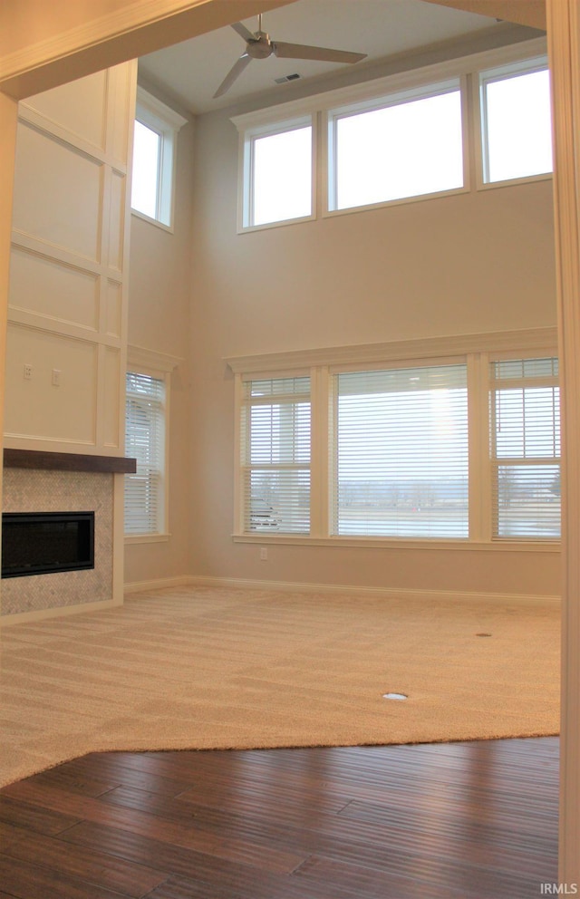 unfurnished living room with hardwood / wood-style floors, a towering ceiling, and ceiling fan