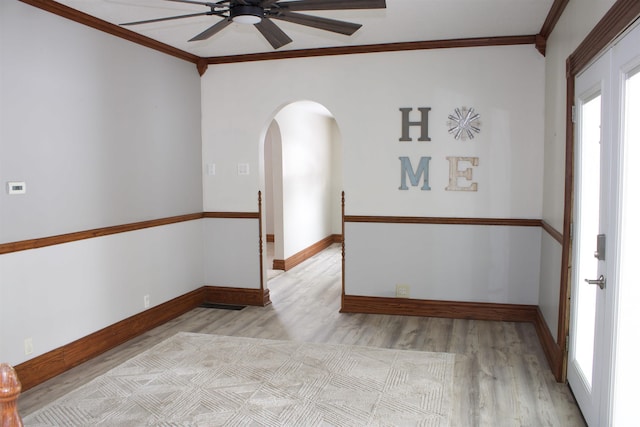 unfurnished room featuring arched walkways, crown molding, baseboards, and light wood-style floors