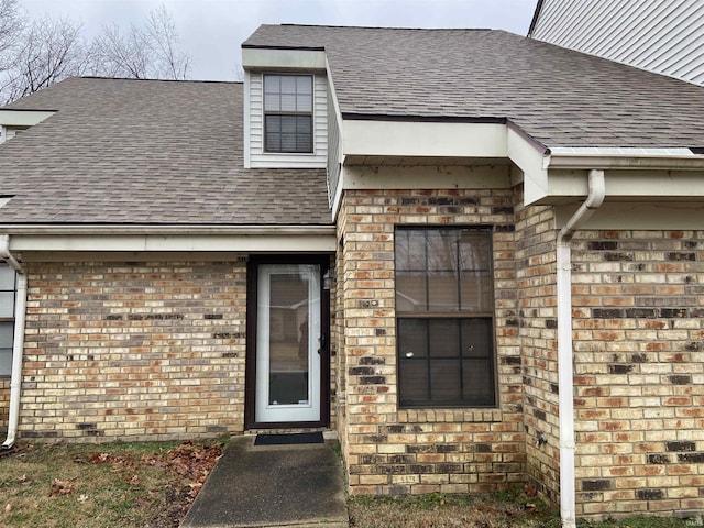 view of exterior entry with roof with shingles and brick siding