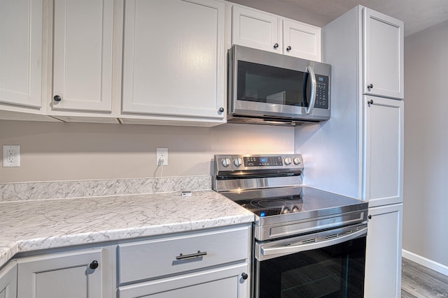 kitchen featuring stainless steel appliances, white cabinets, baseboards, and light stone countertops