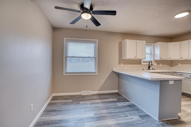 kitchen with light countertops, a peninsula, a sink, and white cabinets