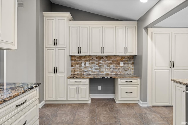 kitchen with white cabinetry, dark stone countertops, vaulted ceiling, and built in desk