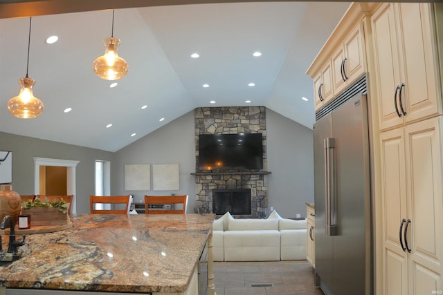 kitchen featuring pendant lighting, stainless steel built in refrigerator, light stone counters, cream cabinets, and a stone fireplace