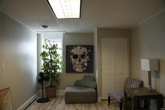 sitting room with crown molding, a drop ceiling, and light hardwood / wood-style flooring