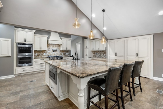 kitchen with white cabinetry, dark stone countertops, appliances with stainless steel finishes, custom range hood, and a large island