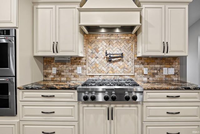 kitchen featuring premium range hood, white cabinetry, tasteful backsplash, dark stone countertops, and appliances with stainless steel finishes