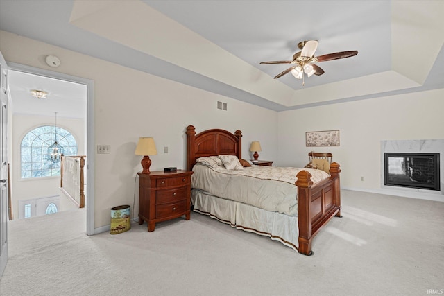 carpeted bedroom with a fireplace, a raised ceiling, and ceiling fan