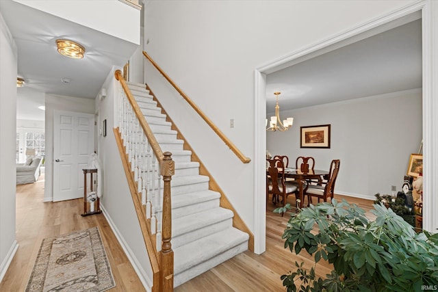 stairs featuring hardwood / wood-style flooring, crown molding, and an inviting chandelier