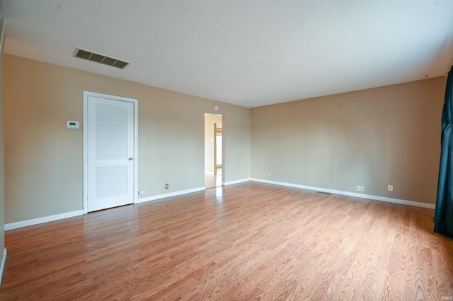 empty room with wood finished floors, visible vents, and baseboards