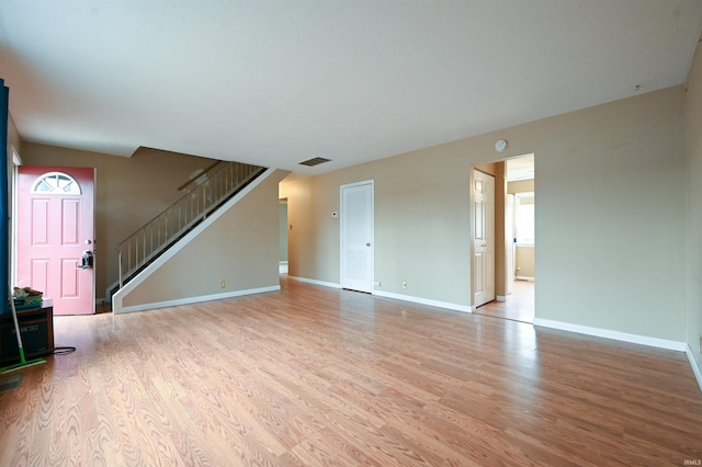 unfurnished living room with stairs, light wood finished floors, visible vents, and baseboards