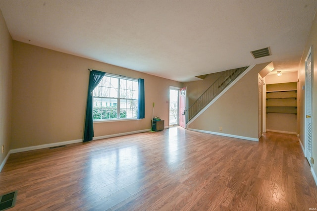 unfurnished living room with wood finished floors, visible vents, and stairs