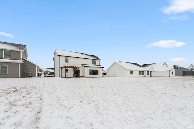 snow covered house with a detached garage and a pergola