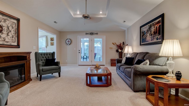 living room featuring light carpet, a tray ceiling, and ceiling fan