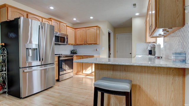 kitchen with a kitchen breakfast bar, kitchen peninsula, stainless steel appliances, light brown cabinets, and light wood-type flooring