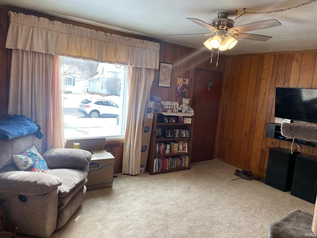 sitting room featuring light carpet, ceiling fan, and wood walls