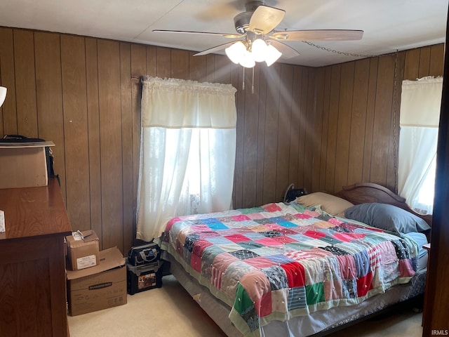 bedroom with multiple windows, light carpet, ceiling fan, and wood walls