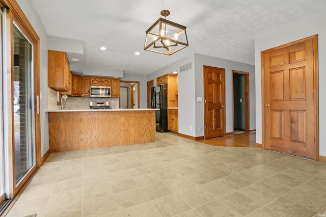 kitchen featuring sink, stainless steel appliances, tasteful backsplash, decorative light fixtures, and kitchen peninsula