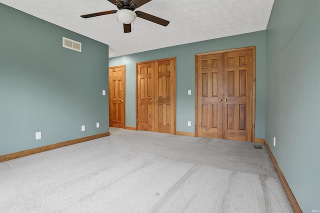 unfurnished bedroom with two closets, ceiling fan, and carpet flooring