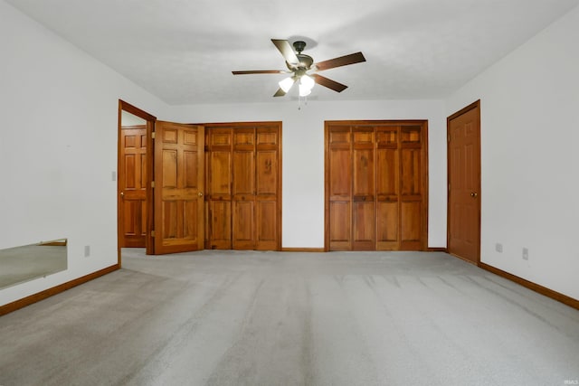 unfurnished bedroom with two closets, light colored carpet, and ceiling fan