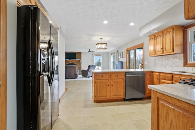 kitchen with pendant lighting, a fireplace, stainless steel dishwasher, kitchen peninsula, and black fridge