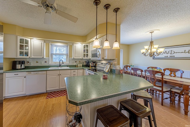 kitchen featuring sink, white cabinets, a kitchen breakfast bar, kitchen peninsula, and white appliances