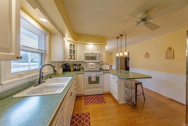 kitchen featuring pendant lighting, sink, white appliances, white cabinets, and kitchen peninsula